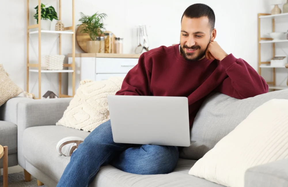 Man sitting on couch smiling using laptop