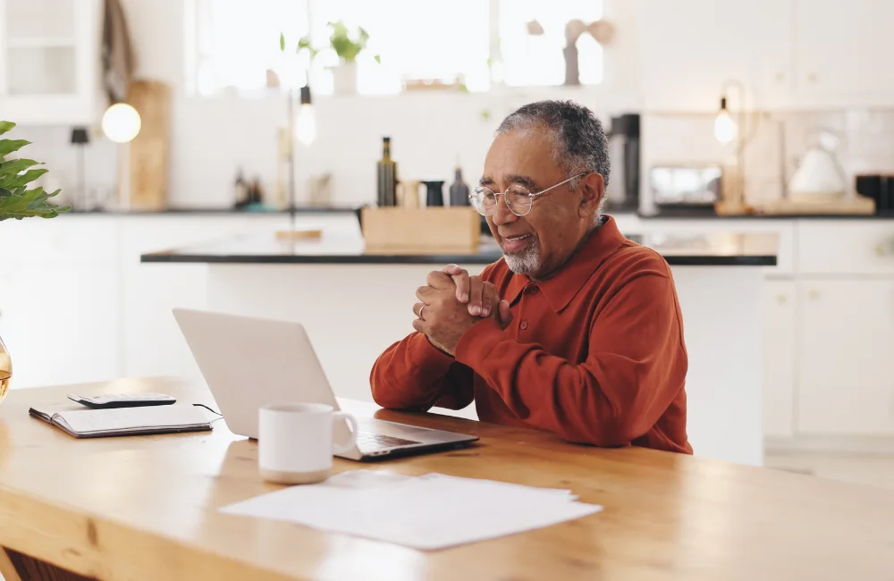 Elderly man sitting at kitchen table using laptop